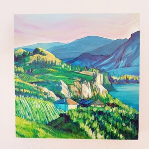 May include: An oil painting of a landscape featuring rolling green hills, a blue lake, and distant mountains under a pink and blue sky. The artwork depicts a vibrant scene with houses and trees.
