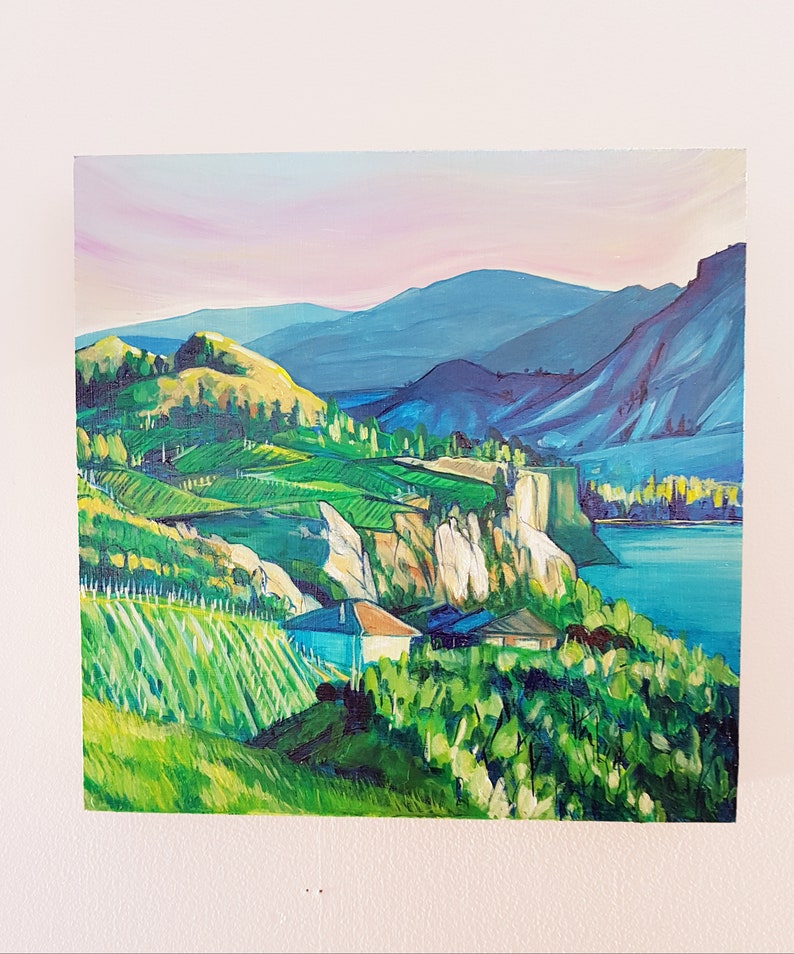 May include: An oil painting of a landscape featuring rolling green hills, a blue lake, and distant mountains under a pink and blue sky. The artwork depicts a vibrant scene with houses and trees.