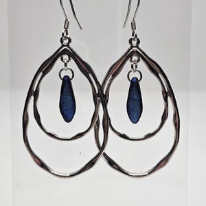 Pode incluir: Brincos de argola de prata com uma conta de vidro azul em forma de lágrima pendurada em cada brinco.