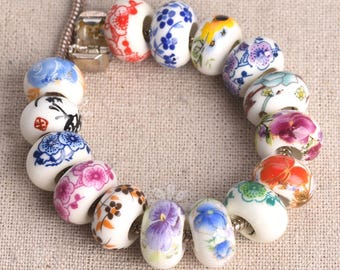 May include: A necklace featuring a series of white ceramic beads, each adorned with a unique floral design in various colors. The beads are strung together, creating a circular arrangement. The designs include red, blue, purple, and orange flowers.