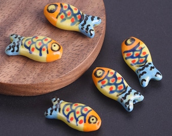 May include: Five ceramic fish figurines. Each fish has a yellow body with orange accents, red and blue patterns, and blue tail fins. The figurines are arranged on a wooden surface.