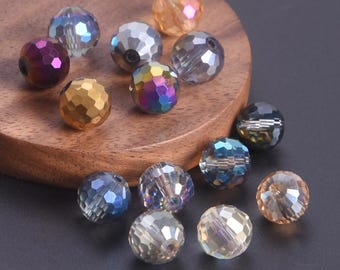 May include: A collection of faceted, round beads in various colors, including gold, purple, blue, and iridescent. The beads are displayed on a wooden surface, with a dark background. These beads are suitable for jewelry making and crafts.