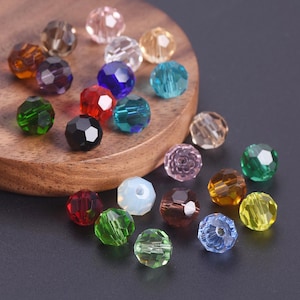 Puede incluir: Una colección de cuentas facetadas en varios colores, incluyendo transparente, ámbar, morado, azul, verde, rojo y negro. Las cuentas están dispuestas sobre una superficie de madera y un fondo oscuro, mostrando su apariencia brillante y similar a una joya. Adecuado para la fabricación de joyas.