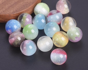 May include: A collection of round, translucent beads featuring internal glitter particles. Each bead displays a unique blend of pastel colors, including pink, blue, green, yellow, and white. The beads have a smooth, glossy finish and a central hole.