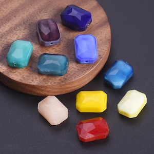 May include: A collection of colorful, faceted gemstone beads in various shapes and sizes. The beads are in shades of blue, green, purple, yellow, red, and cream. They are displayed on a wooden surface and a dark background.