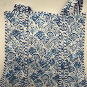 May include: A quilted tote bag with a repeating blue and white seashell pattern. The bag has two blue and white striped handles and a matching border. The design features a variety of stylized fan-shaped shells.