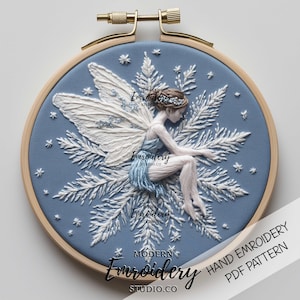 May include: A hand embroidery pattern featuring a fairy sitting on a branch of a wintery tree. The pattern is in a blue and white color scheme and includes snowflakes and stars. The pattern is titled "Modern Embroidery Studio.co" and is available as a PDF download.