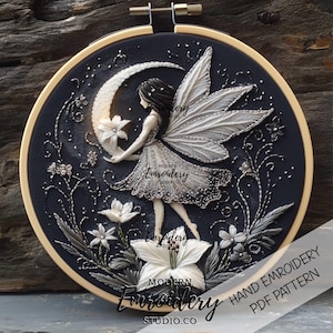 Puede incluir: Un aro de bordado en blanco y negro con un hada sosteniendo una luna creciente y flores. El bordado está sobre tela negra y utiliza hilo blanco. El texto "MODERN EMBROIDERY STUDIO.CO" es visible en la parte inferior del aro.