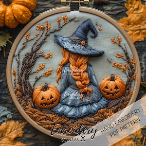 May include: A circular wooden embroidery hoop containing a hand-stitched design of a figure with long orange braided hair wearing a dark blue witch hat and dress, flanked by two orange jack-o'-lanterns, surrounded by brown branches and leaves.