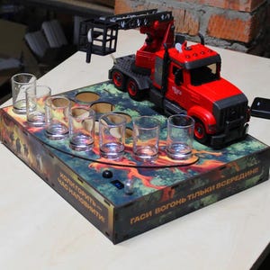 Peut inclure: Un camion jouet rouge avec une grue est posé sur un plateau de service en bois avec six verres à shot. Le plateau présente un motif de forêt en feu et du texte en langue étrangère.