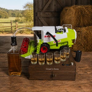 May include: A white and lime green toy combine harvester sits atop a dark wooden box labelled Grant's Farm. A glass bottle of amber liquid is connected to the toy by a clear tube, with six small glasses arranged on the box lid near a black pump.