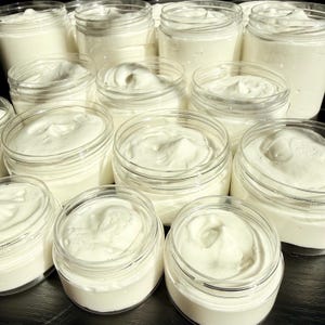 May include: A collection of clear plastic jars filled with a thick, white, creamy substance. Each jar is open, revealing a smooth, whipped texture with soft peaks on the surface. The containers are arranged in a group, showcasing the uniform white color and consistent consistency of the product contained within each individual jar.