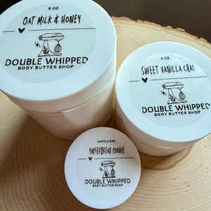 May include: Three round white plastic jars of body butter with white lids. The largest jar is labeled 8 oz Oat Milk & Honey, the medium jar is 4 oz Sweet Vanilla Chai, and the smallest is a sample size Gingerbread Cookie, all with a mixer logo.