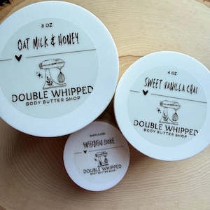 May include: Three white circular containers of body butter with labels. The largest is 8 oz Oat Milk & Honey, the medium is 4 oz Sweet Vanilla Chai, and the smallest is a sample size Gingerbread Cookie. Each label features a stand mixer icon.
