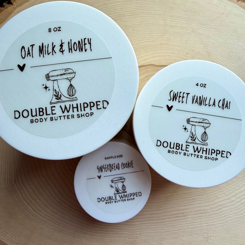 May include: Three white circular containers of body butter with labels. The largest is 8 oz Oat Milk & Honey, the medium is 4 oz Sweet Vanilla Chai, and the smallest is a sample size Gingerbread Cookie. Each label features a stand mixer icon.