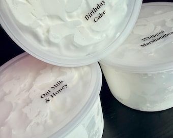May include: Three clear plastic tubs filled with white whipped cream-like substance. Each lid features black text labels reading Birthday Cake, Whipped Marshmallow, and Oat Milk & Honey. The containers are round with smooth, translucent plastic walls.