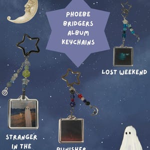 Puede incluir: Tres llaveros cuadrados con portadas de álbumes de Phoebe Bridgers, incluyendo Stranger in the Alps, Punisher y Lost Weekend. Cada llavero tiene una anilla en forma de estrella, cuentas de colores y dijes. El texto dice PHOEBE BRIDGERS ALBUM KEYCHAINS.