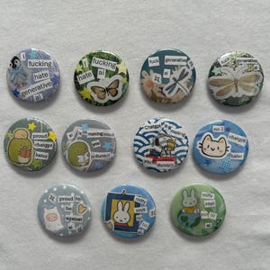 May include: A collection of eleven circular pin-back buttons featuring various cartoon characters, insects, and collage-style text snippets expressing anti-AI sentiments. The designs include illustrations of penguins, butterflies, dragonflies, and rabbits with phrases like I fucking hate generative ai, proud to be against ai, and miffy says no to ai.