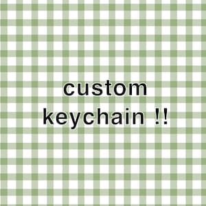 May include: Image features the text "custom keychain !!" in a black font. The background is a green and white gingham pattern. The design is simple and suitable for personalized keychains.