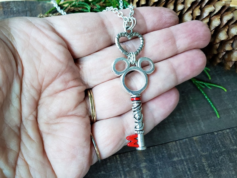 An antique silver key pendant hangs from a silver chain, reminiscent of a Kingdom Hearts keyblade.  Held in an open hand to compare relative size.