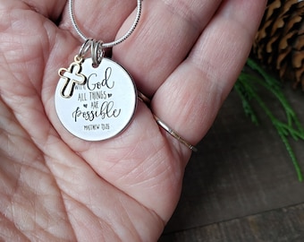 May include: Silver necklace with a round pendant that reads "With God all things are possible Matthew 19:26". The pendant has a small gold cross charm attached to it.