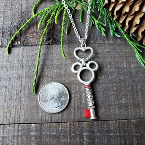 An antique silver key pendant hangs from a silver chain, reminiscent of a Kingdom Hearts keyblade.  Held near a quarter to compare relative size.