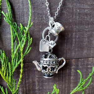 May include: Silver necklace with a teapot charm, a tea bag charm, and a teacup charm. The charms are attached to a silver chain.