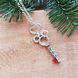 A silver necklace, the pendant is an antique silver key hanging from a silver heart.  The key has mouse ears, and a red M at the bottom.