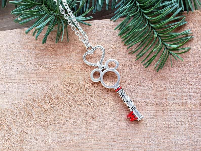 A silver necklace, the pendant is an antique silver key hanging from a silver heart.  The key has mouse ears, and a red M at the bottom.