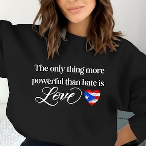 May include: Black sweatshirt with the text "The only thing more powerful than hate is Love" in white script. A heart with the Puerto Rican flag design is next to the word "Love".
