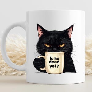 May include: A white ceramic mug with a black handle and the text "But First, Coffee" in a bold, black font. The mug is set against a blurred background, suggesting a cozy setting.
