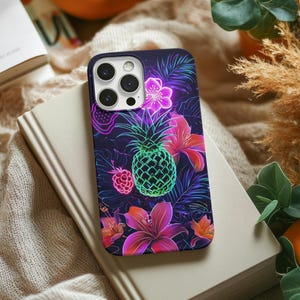 May include: A dark blue phone case with a tropical design. It features a neon green pineapple, pink flowers, and a raspberry against a dark blue leaf background. The case is placed on a book.