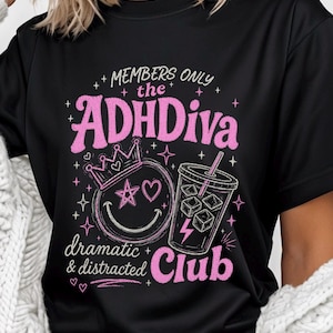 May include: Black t-shirt with a pink graphic that reads "MEMBERS ONLY the ADHDiva Club." The design includes a crown, a smiling face with a star and heart, and a drink with ice cubes. The words "dramatic & distracted" are also included.