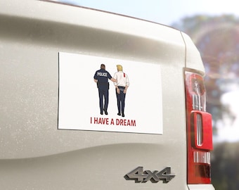 May include: Rectangular white magnet with an illustration of a police officer escorting a person in handcuffs. The text "I HAVE A DREAM" is printed in red below the image. The magnet is affixed to the back of a vehicle.