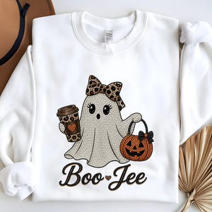 May include: A white crewneck sweatshirt featuring a rhinestone graphic of a ghost wearing a leopard print bow, holding a leopard print coffee cup and an orange jack-o'-lantern bucket. The text "Boo-Jee" is written below in black rhinestones.
