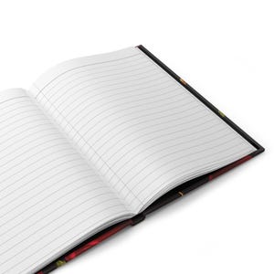 Puede incluir: Un cuaderno abierto con p&aacute;ginas rayadas y una cubierta negra con un dise&ntilde;o floral. La cubierta presenta flores rojas, amarillas y verdes.