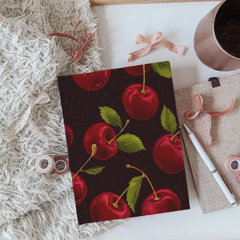 Puede incluir: Una cubierta de cuaderno de color marr&oacute;n oscuro con un patr&oacute;n repetido de cerezas rojas y hojas verdes.