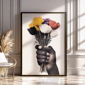 Può includere: Una stampa artistica da parete incorniciata che presenta un'illustrazione in bianco e nero di una mano che tiene un bouquet di fiori vivaci. I fiori includono petali gialli, bianchi, rossi e viola, in contrasto con la mano monocromatica.