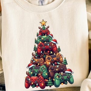 Op de afbeelding: Crèmekleurige sweatshirt met een kerstboomontwerp gemaakt van rode, groene en bruine gamecontrollers. De controllers zijn versierd met kerstmutsen en lichtjes, bekroond met een gouden ster. Een feestelijk kledingstuk met een vakantiethema.