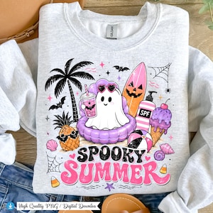 May include: A light grey sweatshirt with a colourful graphic that reads "Spooky Summer." The design features a ghost in sunglasses, a surfboard, ice cream, and a beach ball. Other elements include a palm tree, bats, and a pineapple.