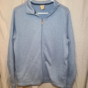 May include: A light blue, heathered knit full-zip jacket with a mock neck collar. The jacket features a central vertical zipper with a brown leather-like pull tab, long sleeves, and a dark blue inner collar lining, all displayed on a white hanger.
