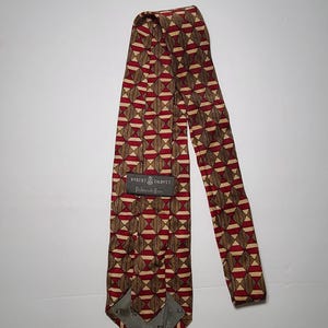 May include: A patterned necktie with a geometric design in shades of brown, red, and beige. The tie features a repeating pattern of diamond and rectangular shapes. The label reads "ROBERT TALBOTT, Redwood Shores".