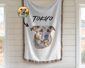 May include: White throw blanket featuring a detailed portrait of a dog with the name "TOKYO" in black script. The blanket has a fringed edge and a smaller inset image of the dog. The dog has brown and tan fur.