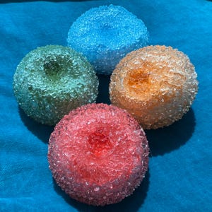 May include: Four colorful, spherical decorative objects. The spheres are in shades of blue, green, orange, and red. Each sphere has a textured, crystalline appearance, and they are arranged on a blue surface.
