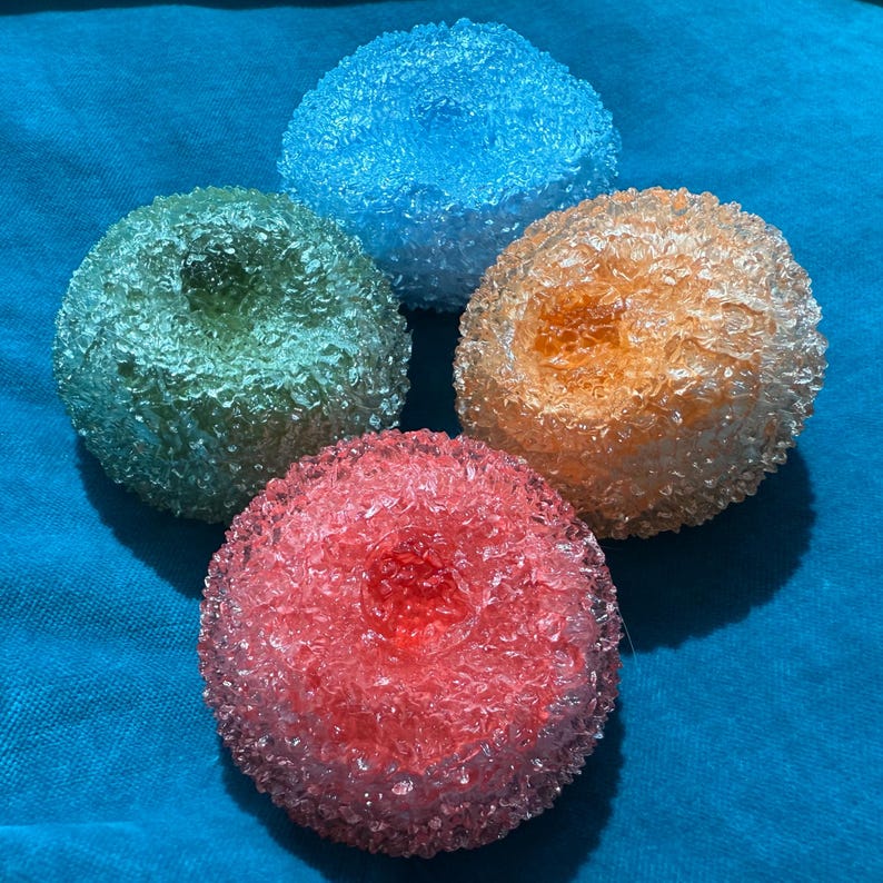 May include: Four colorful, spherical decorative objects. The spheres are in shades of blue, green, orange, and red. Each sphere has a textured, crystalline appearance, and they are arranged on a blue surface.