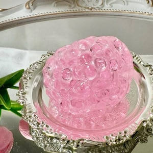 May include: A pink glass sculpture shaped like a cluster of berries, sitting on a silver tray with ornate edges.