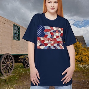 Könnte beinhalten: Marineblaues T-Shirt mit einem Patchwork-Design der amerikanischen Flagge. Das Flaggen-Design enthält Sterne und Streifen mit einem einzigartigen, geometrischen Muster in Rot, Weiß und Blau. Das Shirt ist ein lässiger Stil mit kurzen Ärmeln.