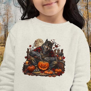 May include: A cream-colored crewneck sweatshirt featuring a graphic print of a werewolf wearing a red and black plaid shirt and brown overalls, carving a jack-o'-lantern. The scene includes autumn leaves, a full moon, and a lantern.