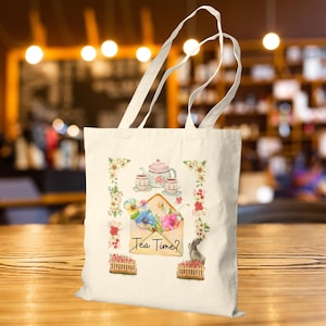 Könnte beinhalten: Cremefarbene Tragetasche mit einem Aquarelldesign. Das Design zeigt eine Teekanne, Teetassen und einen Umschlag mit Blumen. Der Text "Tea Time?" ist auf dem Umschlag aufgedruckt. Blumengrenzen und eine kleine graue Katze vervollständigen das Design.