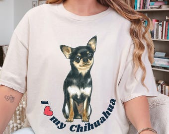 May include: A cream-colored short-sleeve t-shirt featuring a central graphic of a black and tan Chihuahua dog. Below the dog, the text reads "I [heart symbol] my Chihuahua" in dark blue lettering, with the heart symbol in red.